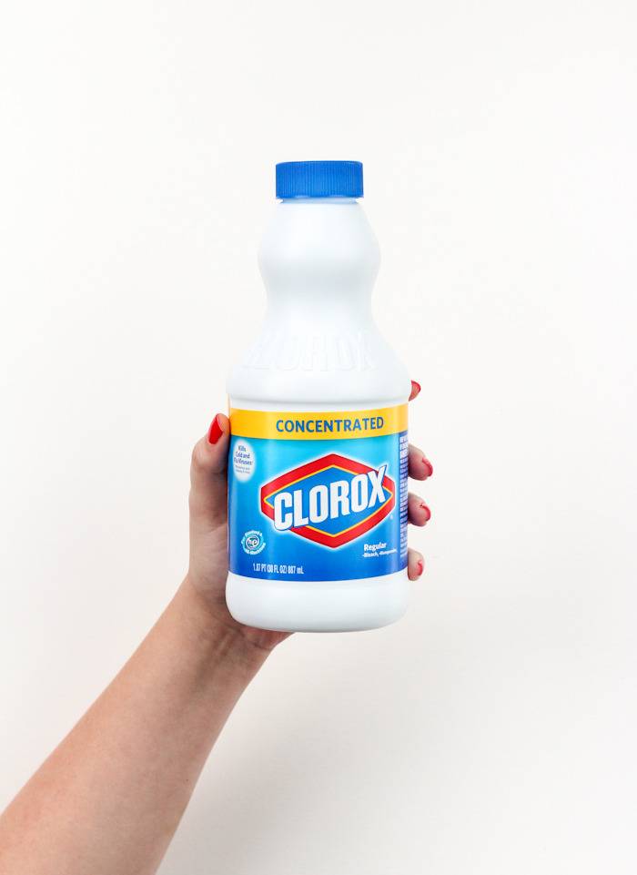 A hand holding up a small bottle of Clorox with a white background.