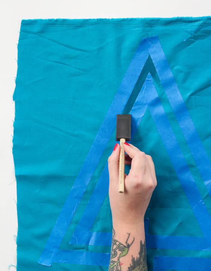 A person uses a black brush on a blue surface.