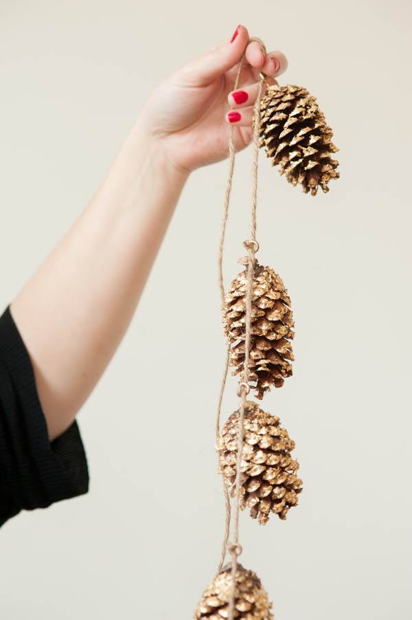 A woman holds up a garland of pine cones.