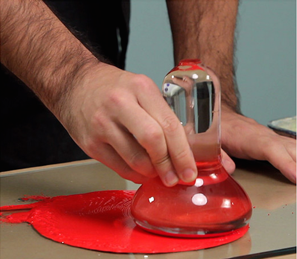 A person is using a glass item on a red material on a counter.