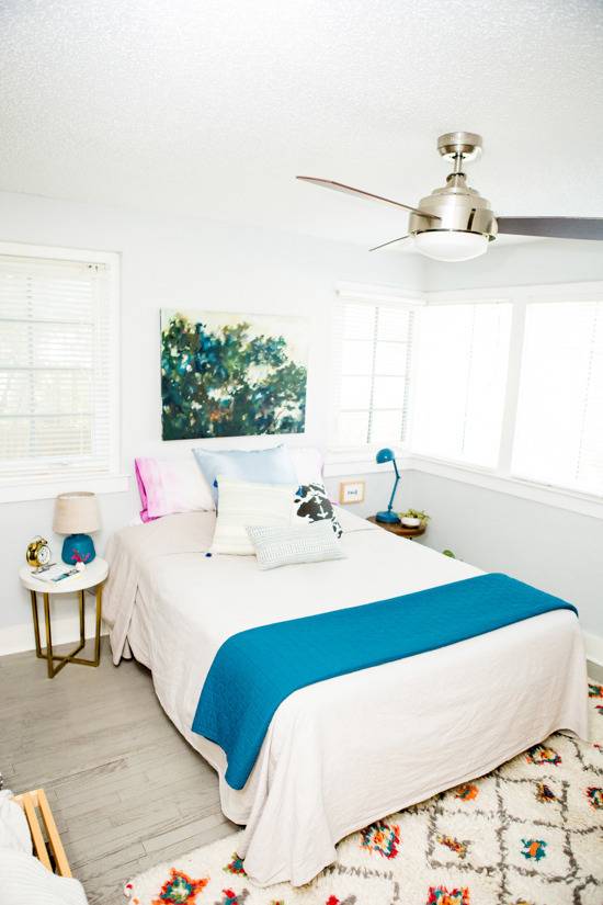 A white and blue sheet is on a bed in a room with a ceiling fan.