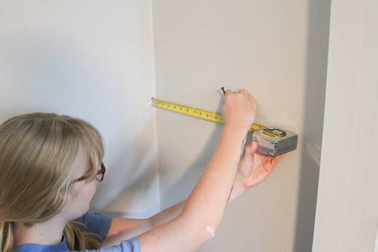 Woman is measuring with a tape measure while holding a nail in her other hand.