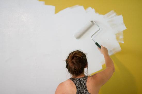 A woman is painting a yellow wall white.