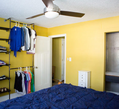 The yellow room has a blue rug and many clothes on shelves.