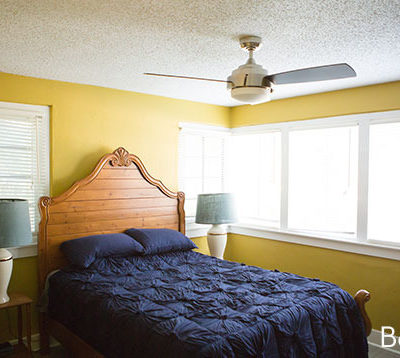 A bedroom with yellow walls and a bed with a blue blanket.