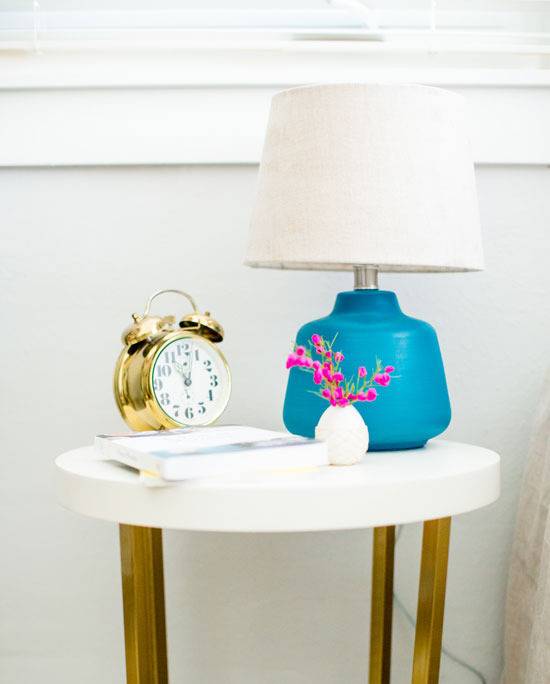 "Night lamp,clock,book and flower pot is on the white wooden table."
