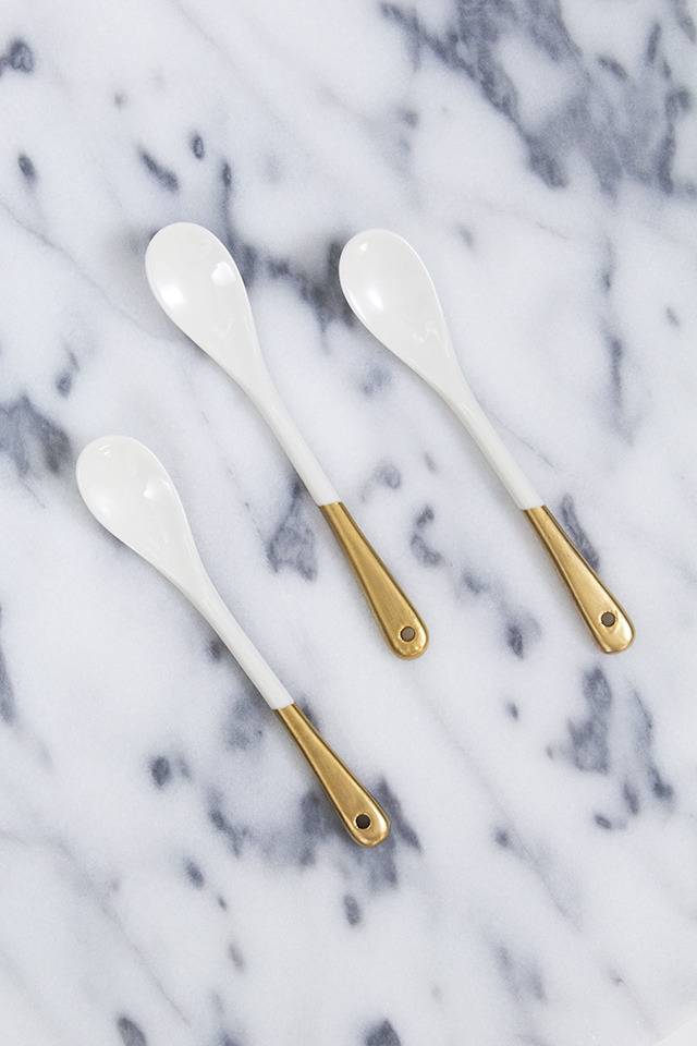White spoons with copper handle tips sit on a white marble countertop.