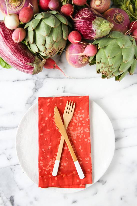 Vegetables create a centerpiece on a table with a red napkin and silverware on top of it sitting on a white plate.