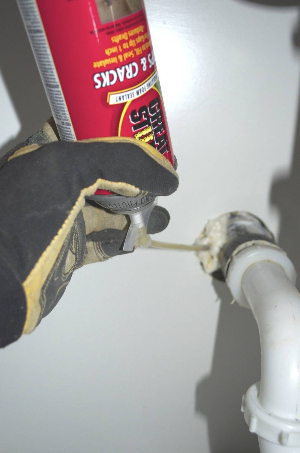 A person uses spray sealer to seal cracks around a pipe.