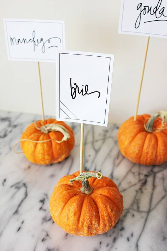 Three mini pumpkins with toothpick signs sticking out of them.