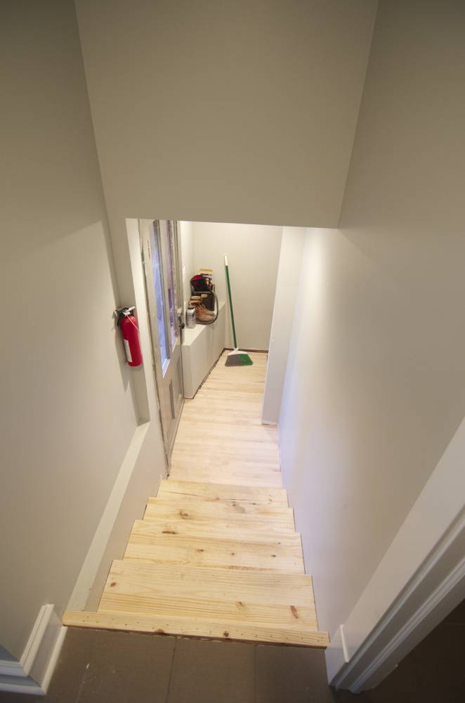 A downward set of raw wooden stairs in a narrow hallway.