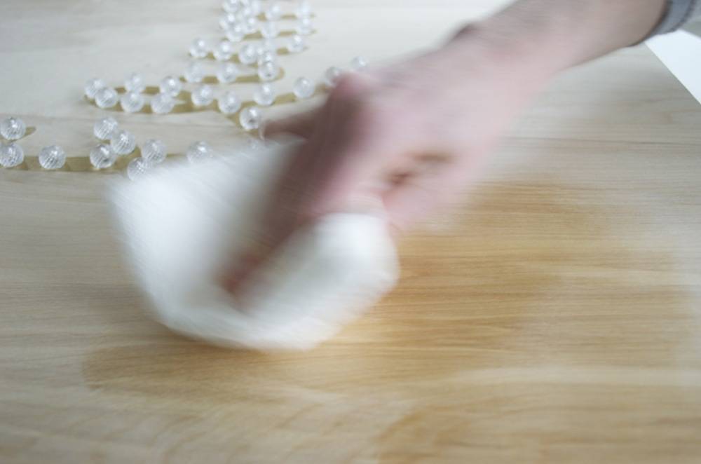 A hand using a white cloth to clean a wooden table.