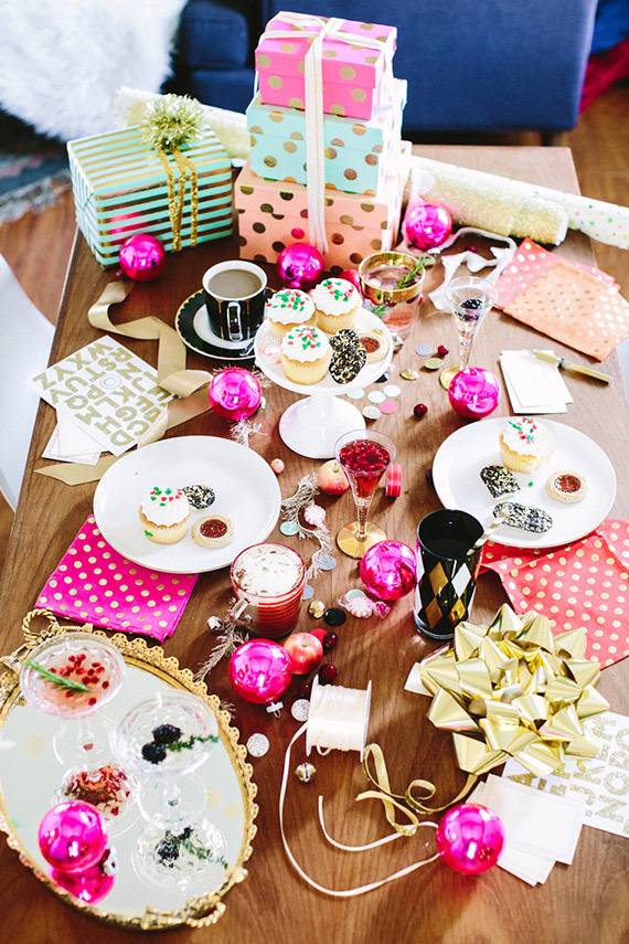 Dinning table filled with gift boxes, decorative items, pink balls,  muffins, coffee mug and gift wraps.