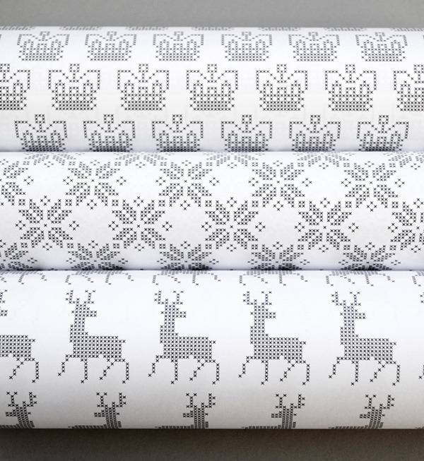 Three rolls of Holiday gift-wrapping, featuring reindeer, snowflake and another design.