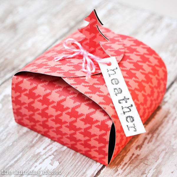 A gift tag reading Heather is on top of a pink and red houndstooth gift box folding closed