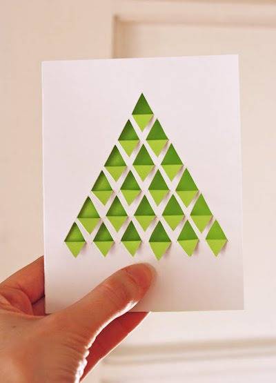 A person holds up a card with a green triangular Christmas tree.