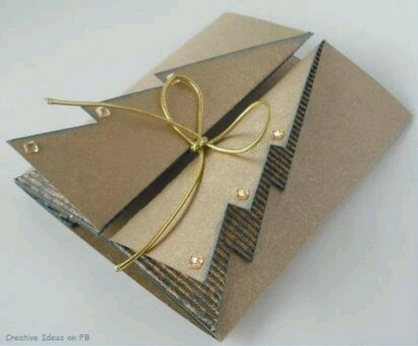 A craft paper card folded to resemble a Christmas tree is tied with thin gold ribbon.