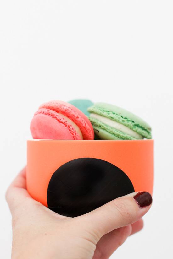 Hand holding orange mug with black dots with no handles with cookies inside.