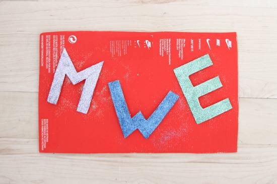 Large cut-out letters m, w, and e rest on a red mat.