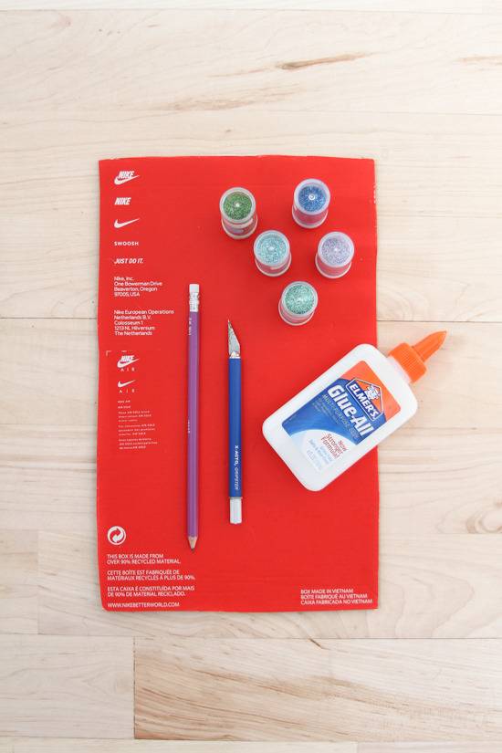 Glue, paint, a pencil and an exacto knife sit on top of a shoebox.