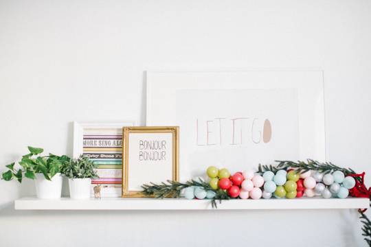 Balls, plants and decorations sit on a white shelf near a white wall.