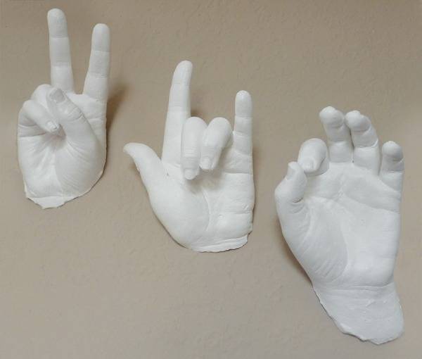 A white hand statue making a piece sign next to a white hand statue making a hang loose sign next to a white hand statue making the okay sign.