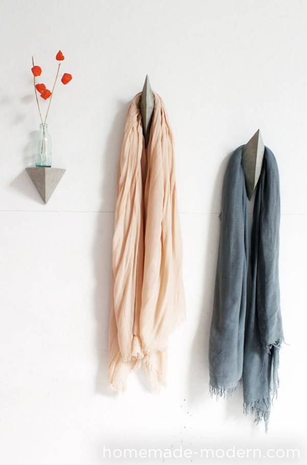 Cloths are hanged to the wall hooks and a flower vase is on the wall.