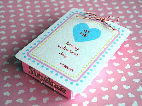 A box with blue dots and a blue hear with the words QT PIE in it laying on a pink table cloth with white hearts.