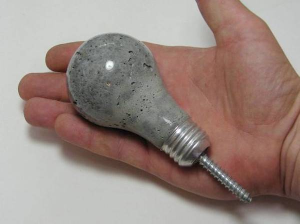 Man holding a grey light bulb in his hand that has a screw coming out of the bottom of it.