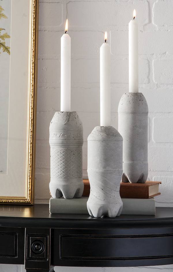 3 concrete Coke bottle shaped candle holders hold white candles.