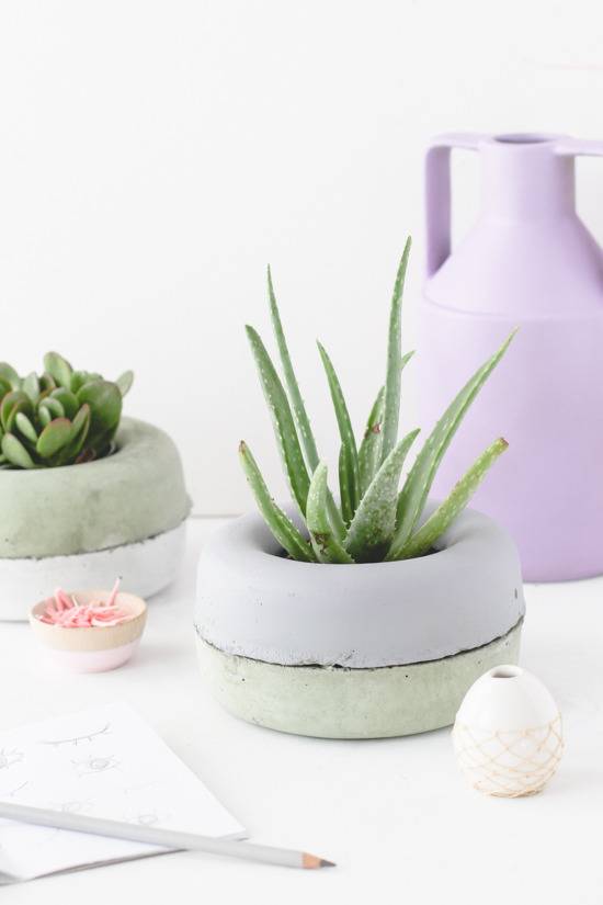 A tall purple vase sits behind two concrete looking plant pots.