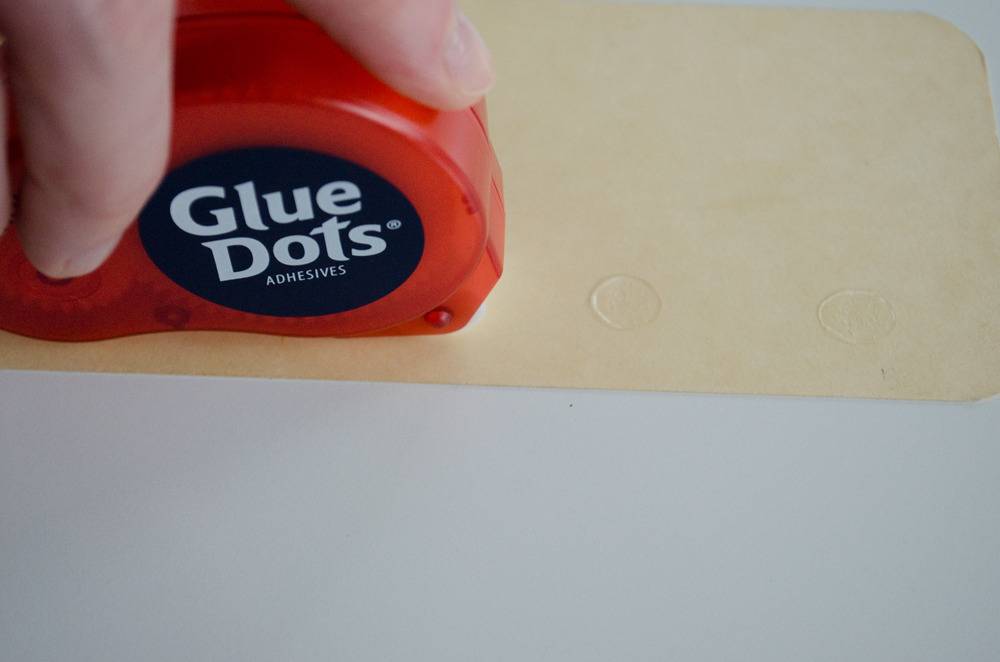 Hand holding a glue dots package on top of manila paper.