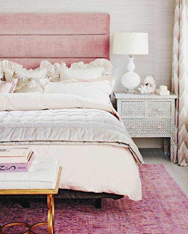 An ornate gold and beige bench siits at the foot of a bed with a pink headboard and a pink carpet.