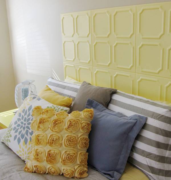 Several pillows are stacked on a bed near a yellow headboard.