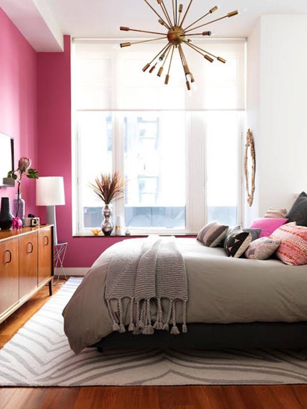 Pink bedroom with bed and designer pillows, cabinet, lamp, and shandler.