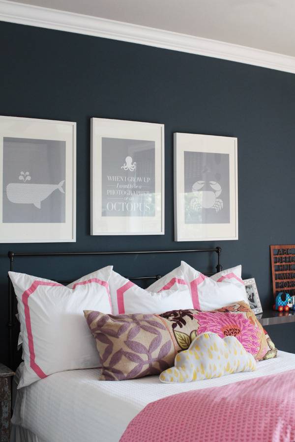 Pink color bed and wall painting frames on black wall.