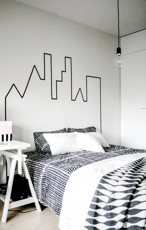 A black and white bedroom with a bed in black and white sheets and cover with a single pendulant light hanging over the bed.