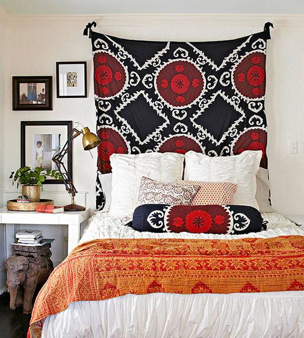A red and black throw hangs on the wall behind a bed.
