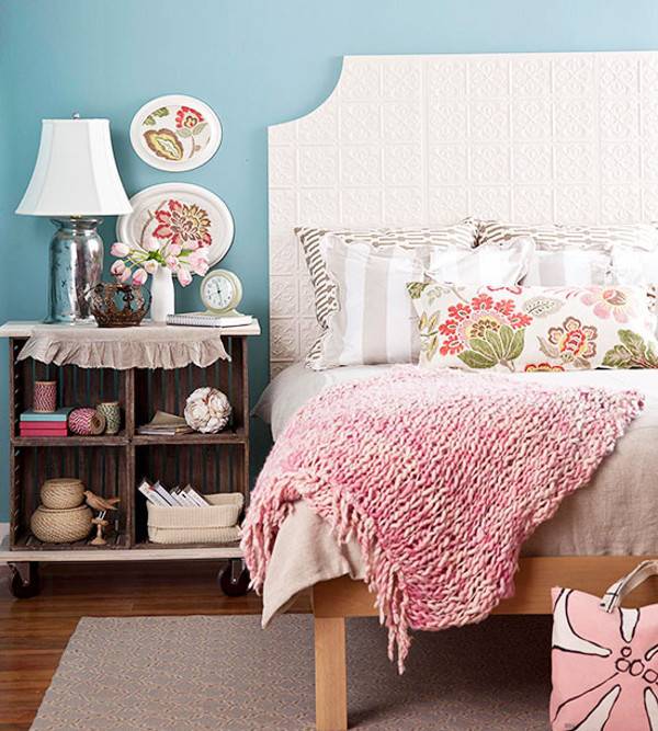 A bed with a pink towel and grey and white striped pillows on it sits next to a nightstand.