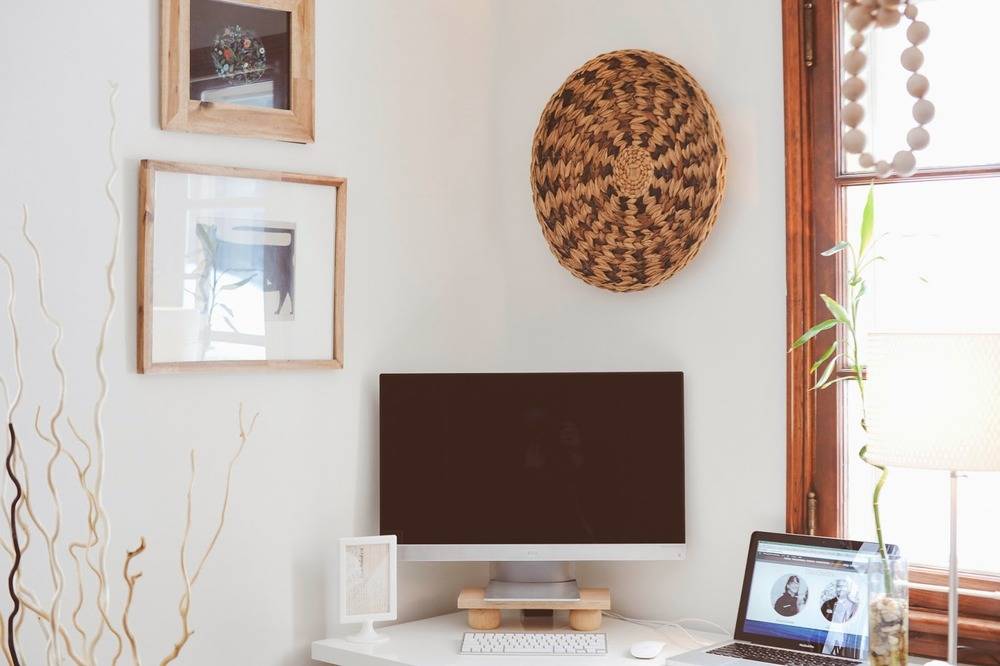 Paintings and artwork are hanging on the wall near a workspace near a window.