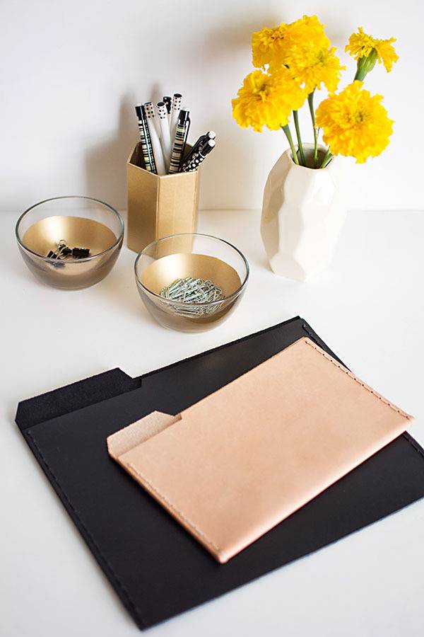 Manila file folders sit on top of black file folders on a white desk with pretty yellow flowers on it.