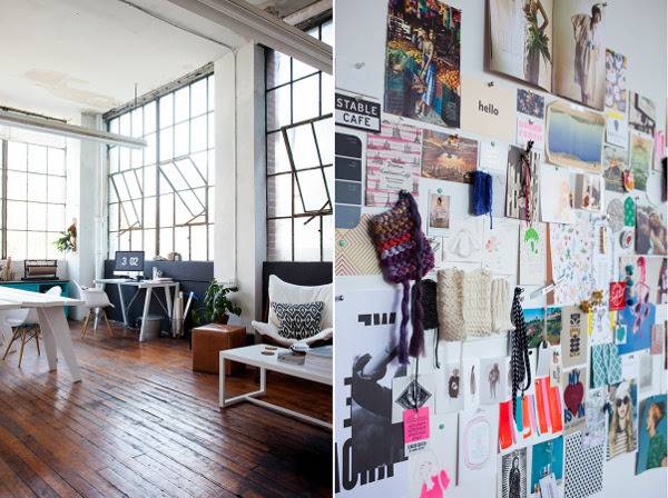 Loft with wall of windows and wooden furniture with a collage of papers on wall.