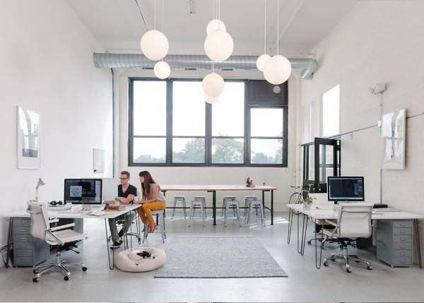 Open design studio with high ceilings and wooden floor filled with work stations.