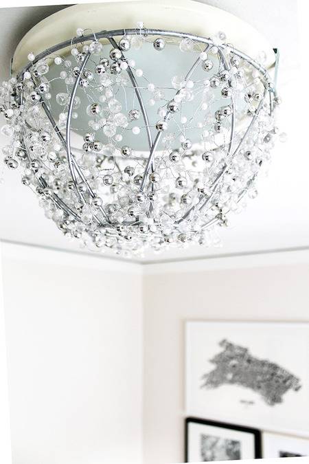 A light with flowers are above pictures on the wall.