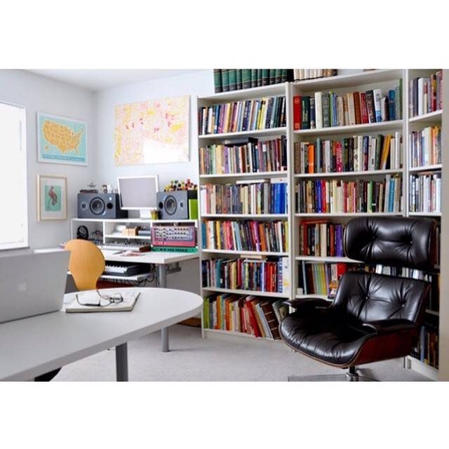 A home office with a black chair and a wall book shelf filled with books.