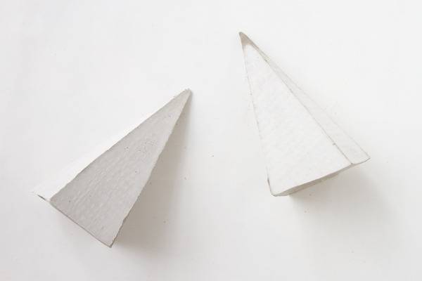 Two white, triangular, geometric bookends lie on a surface.