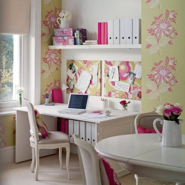 Paper is stuck to a wall with decorative flowers all over it above a white desk next to a white table.