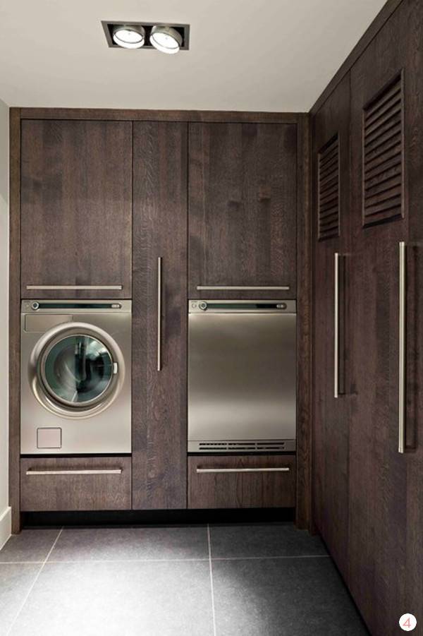 Stainless steel washer and driver mounted into dark wood cabinets in a laundry room.