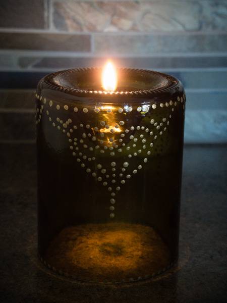 A patterned candle holder has a candle burning in it.