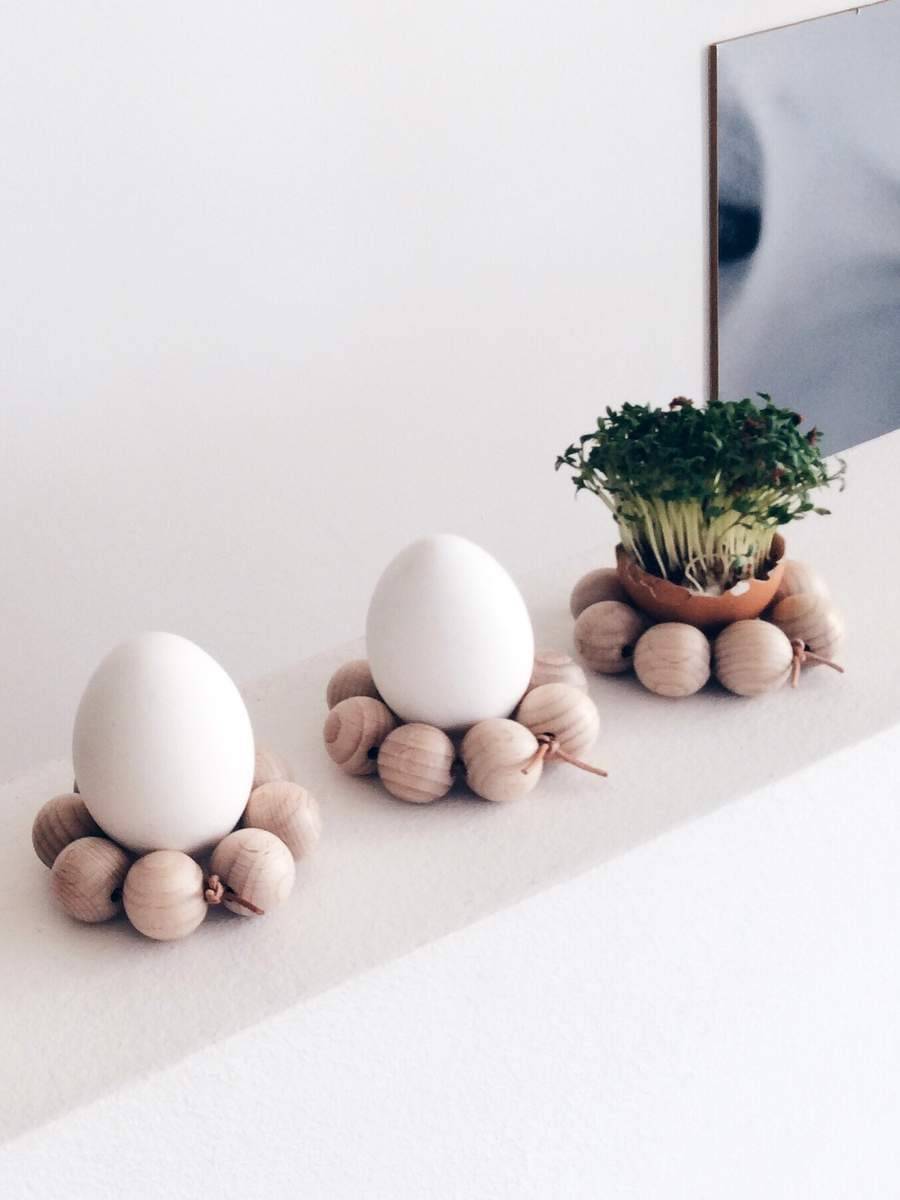 Two eggs sit on pedestals made from round wooden balls next to a small potted plant.